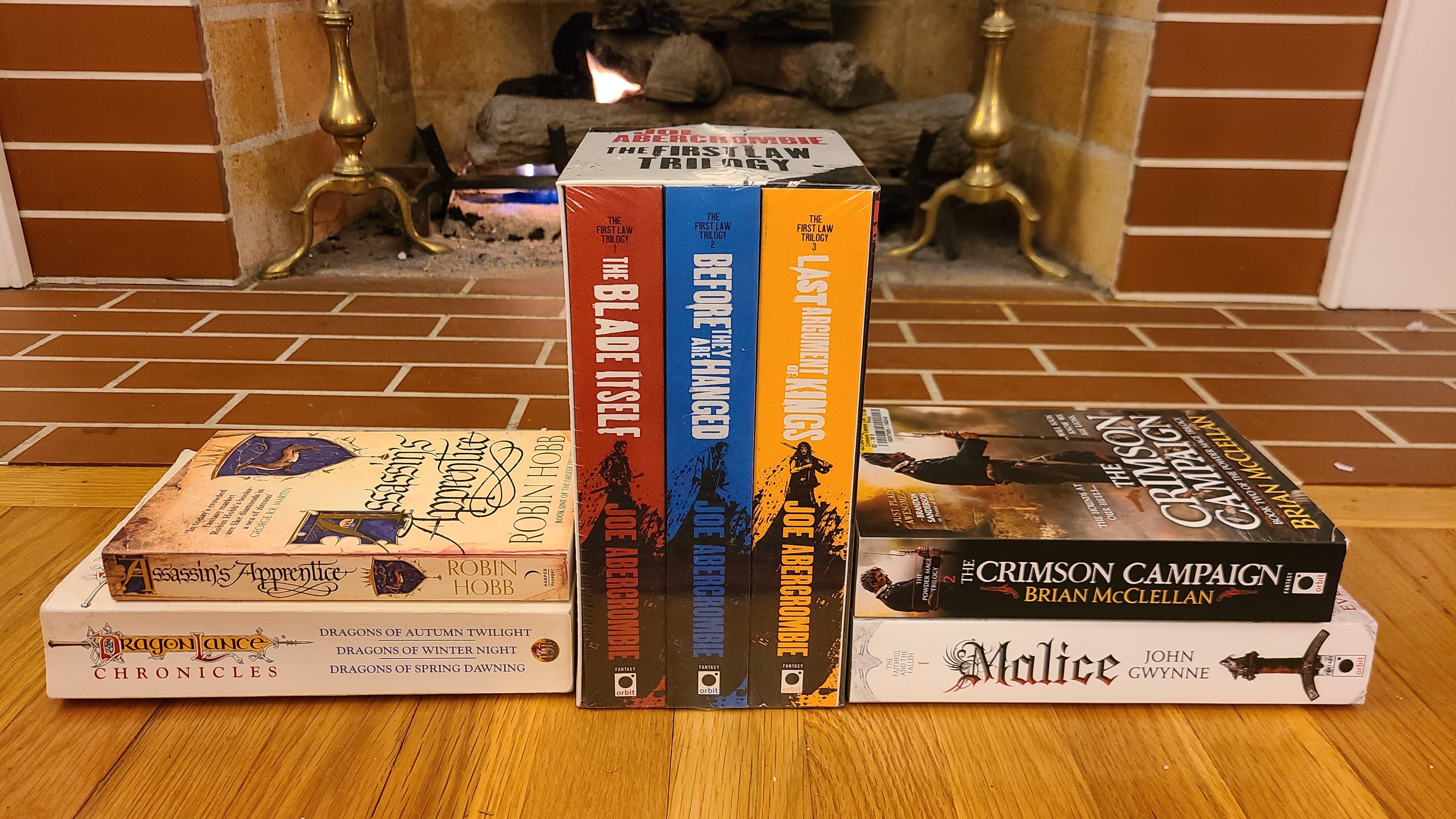 Pic of books in front of fireplace. Includes Assassin's Apprentice, Dragonlance Chronicles, The First Law Trilogy, The Crimson Campaign, and Malice